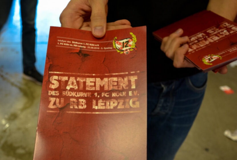 Hand hält Flyer mit Statement der Südkurve 1. FC Köln zu RB Leipzig.